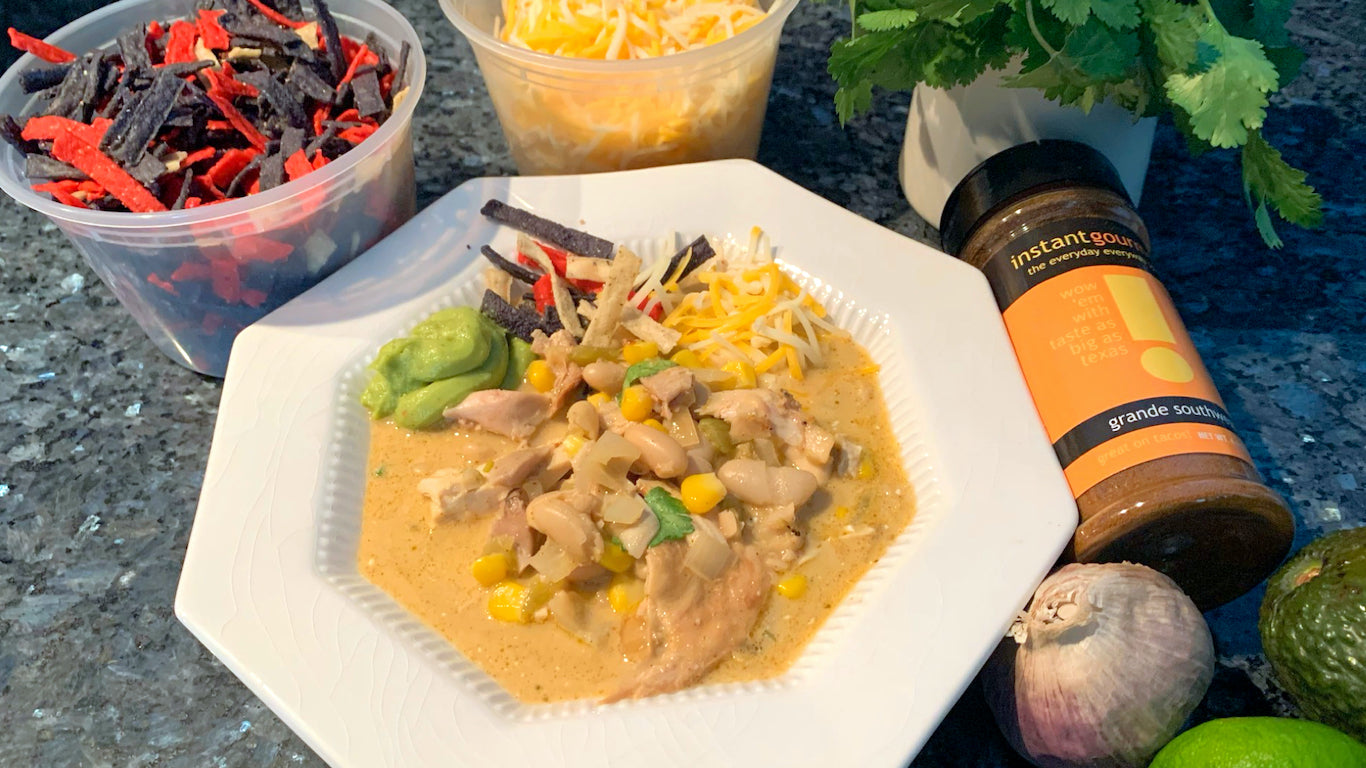 Bowl of White Chicken Chili made with Instant Gourmet Grande southwest seasoning blend. Chili includes meaty chicken, corn, cilantro in a creamy broth;garnished with avocado, tortilla strips and cheese.