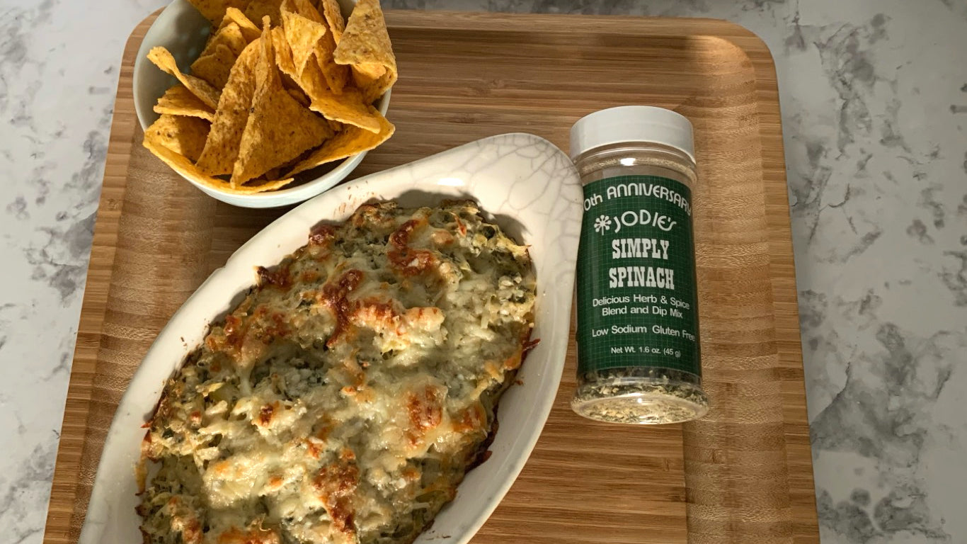 picture of baked spinach artichoke dip with tortilla chips and a bottle of the simply spinach seasoning blend bottle