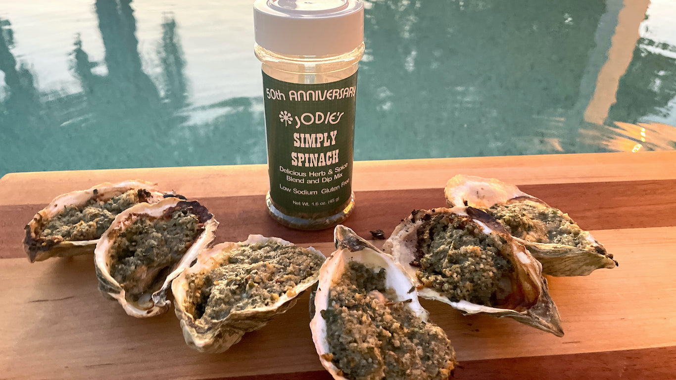 Grilled oysters in shell on cutting board with bottle of simply spinach in background